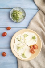 White cheese with tomatoes and cilantro microgreen on blue wooden background and linen textile. top