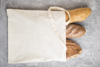 Reusable textile grocery bag with fresh baked bread on a gray concrete background. top view, flat