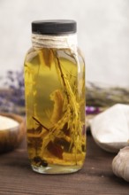 Sunflower oil in a glass jar with various herbs and spices, lavender, sesame, rosemary on a brown