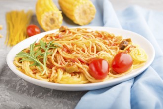 Corn noodles with tomato sauce and arugula on a gray concrete background and blue textile. Side