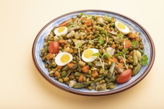 Mung bean porridge with quail eggs, tomatoes and microgreen sprouts on a pastel orange background.