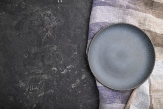 Empty blue ceramic plate on black concrete background and linen textile. Top view, copy space, flat