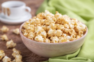 Popcorn with caramel in ceramic bowl on brown concrete background and green textile. Side view,