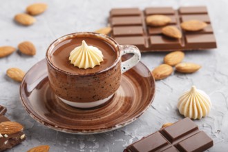 Cup of hot chocolate and pieces of milk chocolate with almonds on a gray concrete background. side