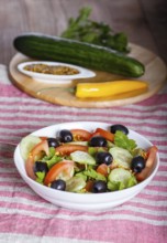 Vegetarian salad of tomatoes, cucumbers, parsley, olives and mustard on linen tablecloth, close up,