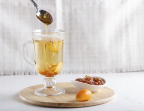 Jasmine tea with kumquat in a glass cup and a spoon with jam, on a wooden board on a white