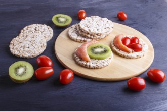 Rice cakes with salmon, kiwi and cherry tomatoes on dark wooden background. close up