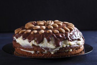 Homemade chocolate cake with milk cream and almonds on black wooden background. close up