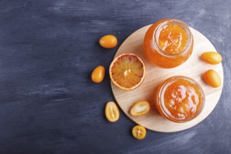 Orange and kumquat jam in a glass jar with fresh fruits on black wooden background. Homemade, top