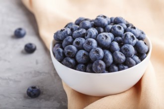 Fresh blueberry in white bowl and orange pastel textile on gray concrete background. side view,