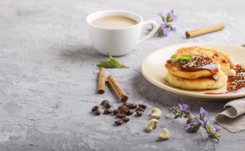 Cheese pancakes with caramel sauce on a beige ceramic plate and a cup of coffee on a gray concrete