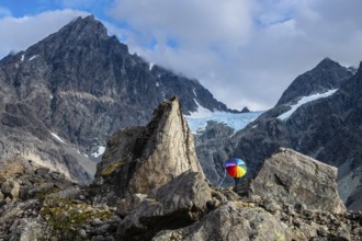 Woman with colorful open umbrella between large rocks, glacier Lenangsbreen, at glacier lake