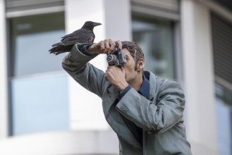 Real crow on a pillar saint, The Photographer, in front of the main railway station in Düsseldorf,