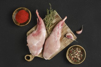 Two whole rabbit legs sit on a wooden cutting board alongside garlic, fresh thyme, and bowls of