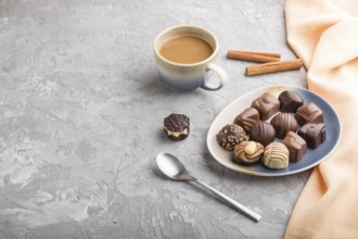 Different chocolate candies and a cup of coffee on a gray concrete background and orange textile.