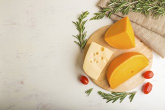 Various types of cheese with rosemary and tomatoes on wooden board on a white wooden background and