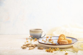 Orange macarons or macaroons cakes with cup of coffee on a white concrete background and linen