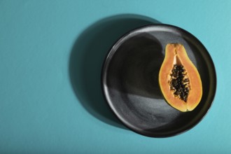 Ripe cut papaya on gray plate on blue pastel background. Top view, flat lay, copy space, hard light