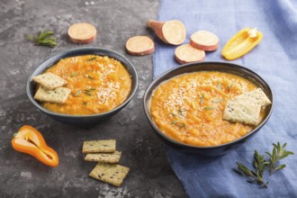 Sweet potato or batata cream soup with sesame seeds and snacks in blue ceramic bowls on a black