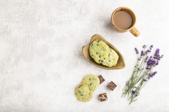 Green cookies with chocolate and mint on leaflike ceramic plate with cup of coffee on gray concrete