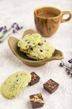 Green cookies with chocolate and mint on leaflike ceramic plate with cup of coffee on gray concrete