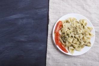 Farfalle pasta with pesto sauce, tomatoes and cheese on a linen tablecloth on black wooden