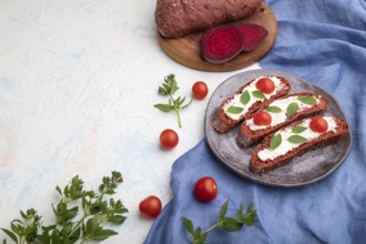 Red beet bread sandwiches with cream cheese and tomatoes on white concrete background and blue