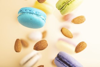 Multicolored flying macaroons and almonds frozen in the air on blurred beige background. top view,