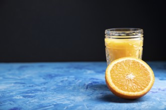 Glass of orange juice on a black and blue background. Hard light, contrast. Side view, copy space