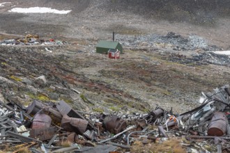 Cabin near scrap yard in rocky, hilly landscape with snow remains, arctic settlement