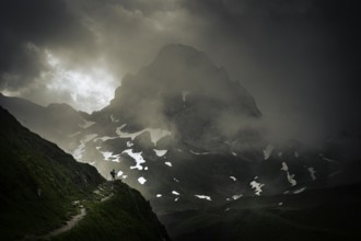 Mountaineer on a path with summit in the morning light and dramatic clouds, Lech,