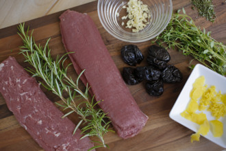 Swabian cuisine, preparation of lamb with prunes, raw lamb, rosemary, herbs, sliced garlic, lemon