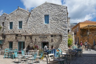 People relaxing in a terrace café in front of a traditional stone house with blue shutters, Old