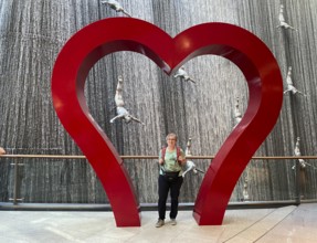 Interior shot, best ager, elderly woman, standing in frame, heart, in front of The Waterfall,