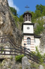 Bell tower with clock and cross surrounded by stairs and blue sky, Bulgarian Orthodox cave