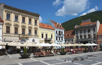 People sitting in outdoor cafés in front of historical buildings on a sunny day in a city, town