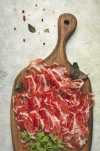 Prosciutto on a cutting board, top view, appetizer, breakfast, spices and herbs