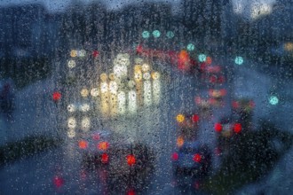 Rainy weather, road traffic, raindrops on a window pane, behind, blurred, lights of vehicles on a