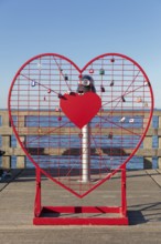 A red heart with padlocks stands on the pier in front of the blue sea horizon, Rügen, Binz