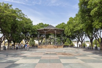 A pavilion under trees in a park with people walking by, Jerez