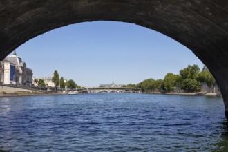 View through an arched bridge onto a river with a city background, Paris