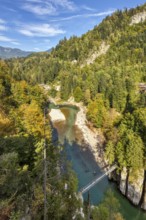 View of a river meandering through the wooded mountains, a suspension bridge spans the river,