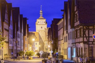 Galgengasse and White Tower in the old town of Rothenburg ob der Tauber, illuminated at night.