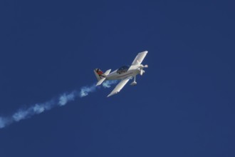 Stunt aerobatic plane performing stunts in blue sky with smoke trail. Concept of speed, difficulty,