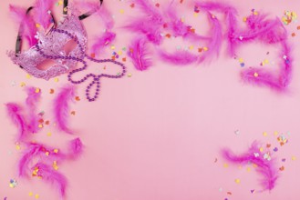 Pink mask with feathers and confetti on a pink background, playful and cheerful atmosphere