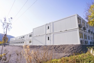 White container houses outside under a clear sky, modern construction, quiet surroundings, refugee