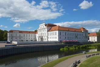 A large baroque palace with red roofs next to a peaceful river and park, Oranienburg Palace,