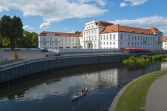 A baroque castle on the water with canoeists and a terrace with a red roof, Oranienburg Castle,