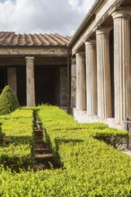 Large old building structure with columns and inner garden courtyard with a maze of trimmed hedges