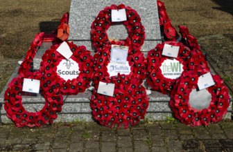 Poppy wreaths at base of war memorial remembrance monument, Saxmundham, Suffolk, England, UK